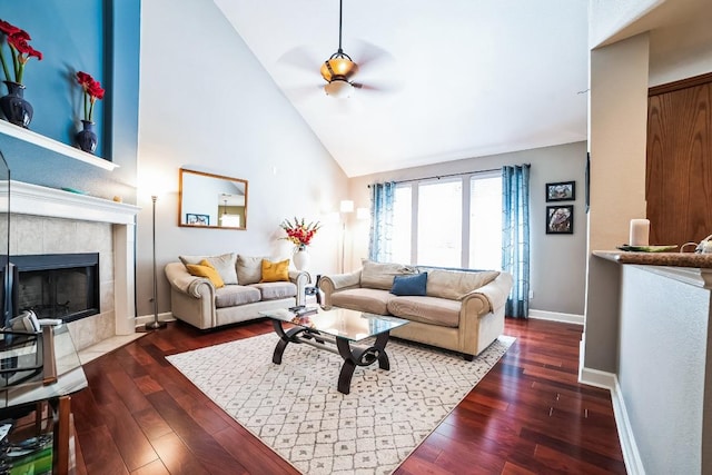 living room featuring high vaulted ceiling, a tile fireplace, baseboards, and wood finished floors