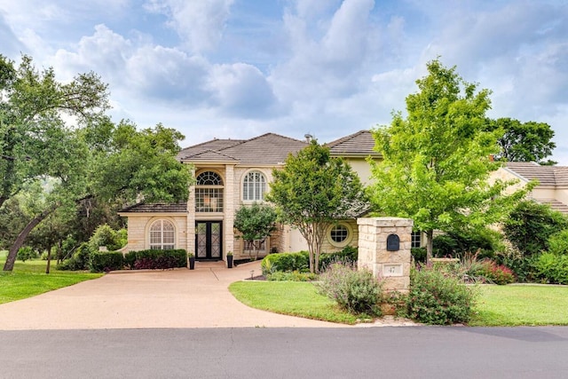 mediterranean / spanish home featuring concrete driveway, french doors, a front lawn, and stone siding