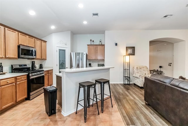 kitchen featuring visible vents, arched walkways, open floor plan, stainless steel appliances, and a kitchen bar