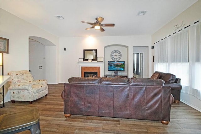 living area with visible vents, a tiled fireplace, and wood finished floors