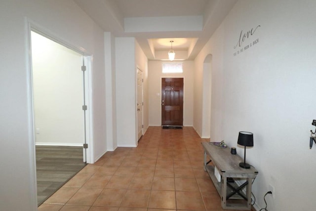 hallway featuring a tray ceiling, light tile patterned flooring, arched walkways, and baseboards