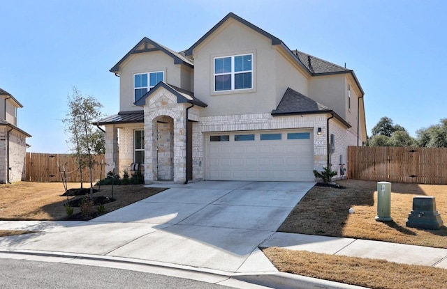 view of front facade featuring driveway, stone siding, roof with shingles, fence, and stucco siding