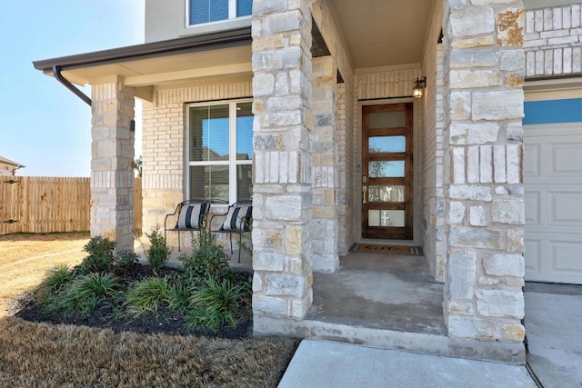 entrance to property with stone siding, brick siding, a porch, and fence