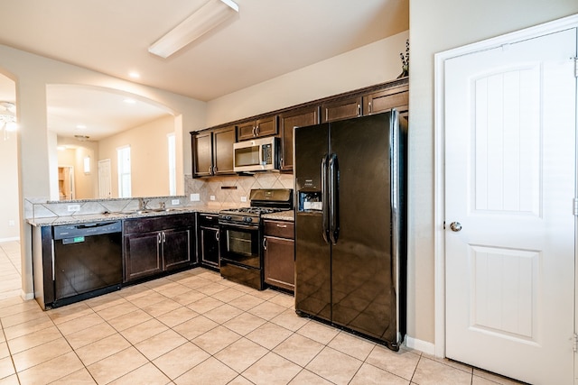 kitchen featuring arched walkways, a sink, dark brown cabinetry, black appliances, and backsplash