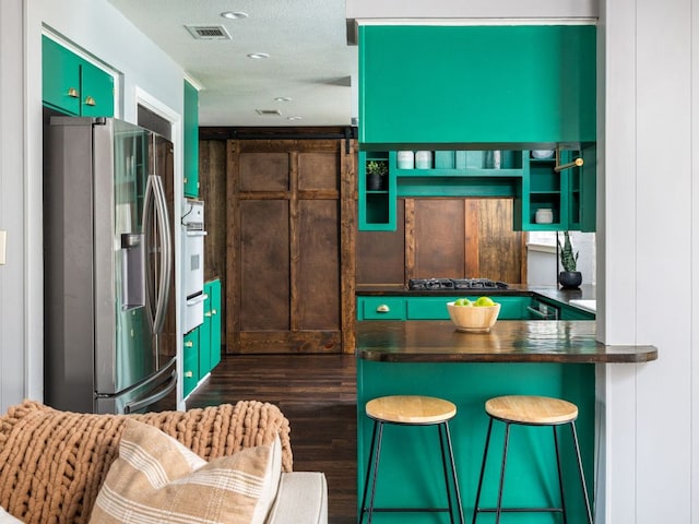 kitchen featuring gas stovetop, dark countertops, visible vents, oven, and stainless steel fridge with ice dispenser