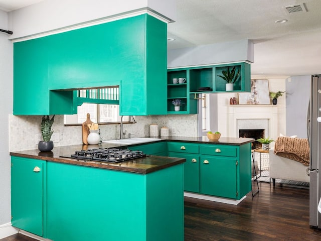 kitchen with gas cooktop, a peninsula, a sink, green cabinets, and dark countertops