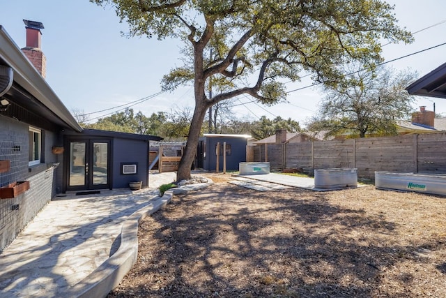 view of yard with an outbuilding, french doors, a patio, a storage shed, and fence