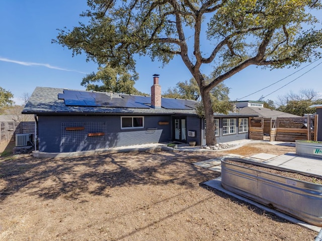 back of house with brick siding, a chimney, fence, and roof mounted solar panels