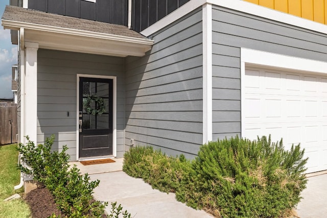 property entrance featuring a garage, a shingled roof, board and batten siding, and fence