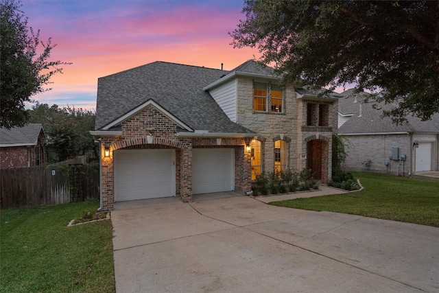 view of front of home with a shingled roof, a lawn, an attached garage, fence, and stone siding