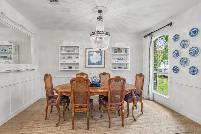 dining room with wainscoting, a decorative wall, plenty of natural light, and an inviting chandelier