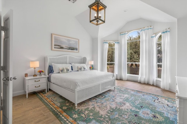 bedroom featuring a notable chandelier, lofted ceiling, visible vents, wood finished floors, and baseboards