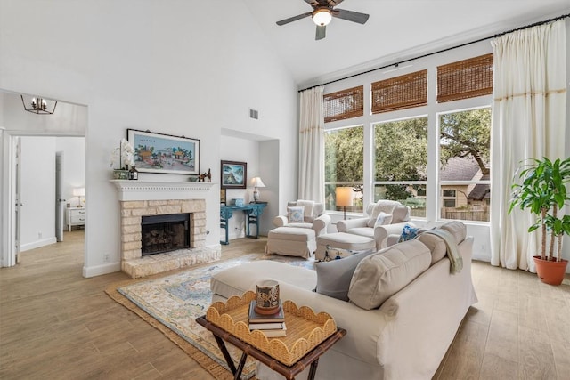 living area with light wood finished floors, visible vents, a fireplace, high vaulted ceiling, and ceiling fan with notable chandelier