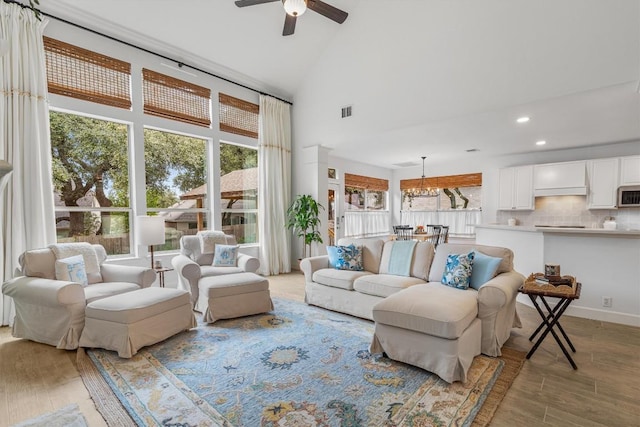 living area featuring high vaulted ceiling, light wood-style flooring, recessed lighting, ceiling fan with notable chandelier, and visible vents