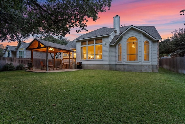 back of property with roof with shingles, a chimney, a lawn, a patio area, and a fenced backyard