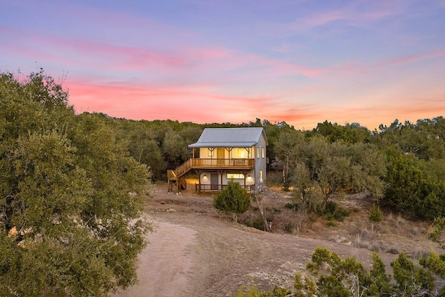 view of front of property with dirt driveway, metal roof, stairway, and a wooded view