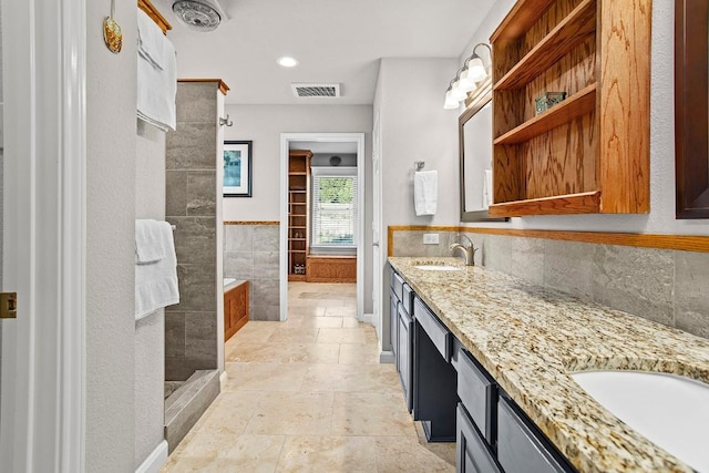 full bath featuring a sink, visible vents, tiled shower, double vanity, and stone tile flooring