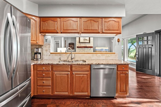 kitchen featuring tasteful backsplash, dark wood-style floors, light stone countertops, stainless steel appliances, and a sink