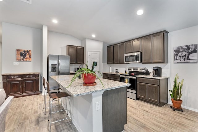 20602 Falcon, Lago Vista, TX 78645 - kitchen featuring appliances with stainless steel finishes, dark brown cabinetry, light wood-style floors, light stone counters, and a kitchen island with sink