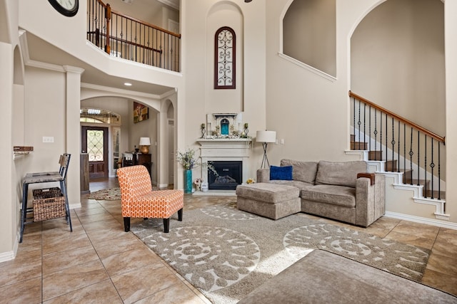 tiled living room featuring baseboards, stairs, a high ceiling, arched walkways, and a glass covered fireplace