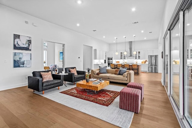 living room featuring a high ceiling, light wood-type flooring, visible vents, and recessed lighting