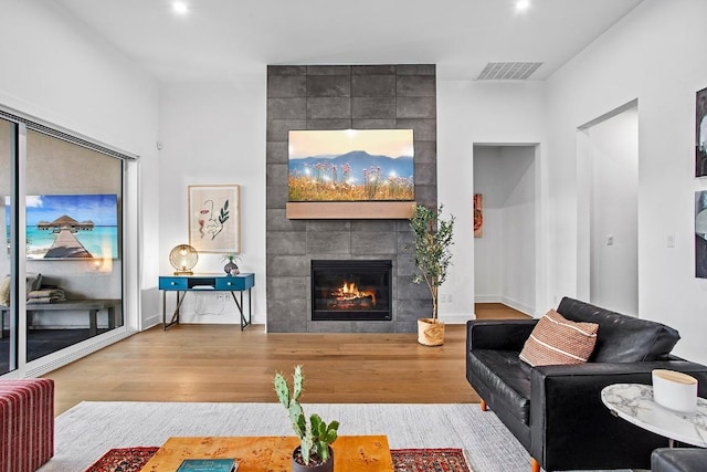 living area featuring a tile fireplace, visible vents, recessed lighting, and wood finished floors