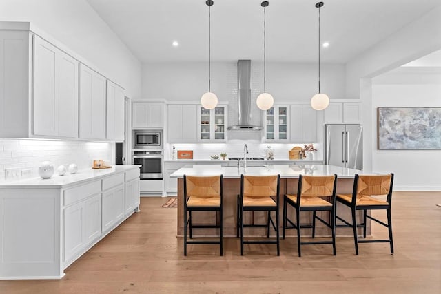 kitchen with light wood-style floors, wall chimney exhaust hood, appliances with stainless steel finishes, and light countertops