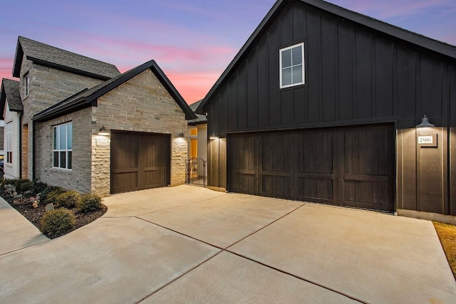 view of front facade with driveway, stone siding, a garage, and board and batten siding