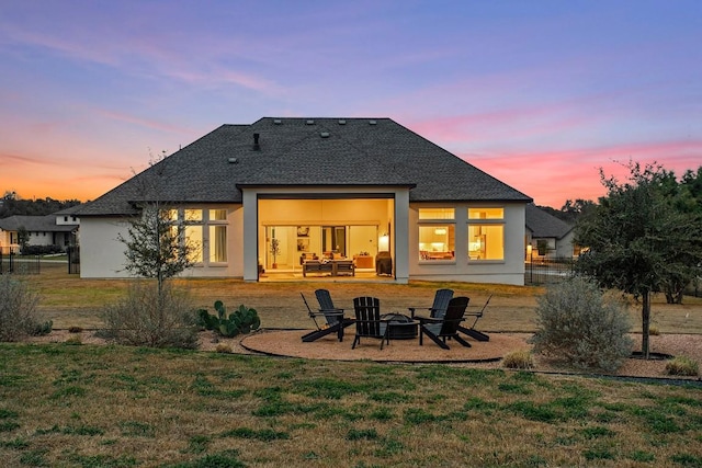 rear view of property featuring roof with shingles, a lawn, stucco siding, a patio area, and an outdoor living space with a fire pit