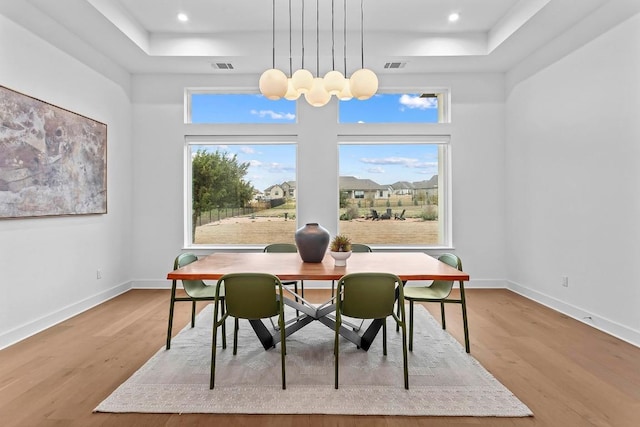 dining room with wood finished floors, a raised ceiling, visible vents, and baseboards