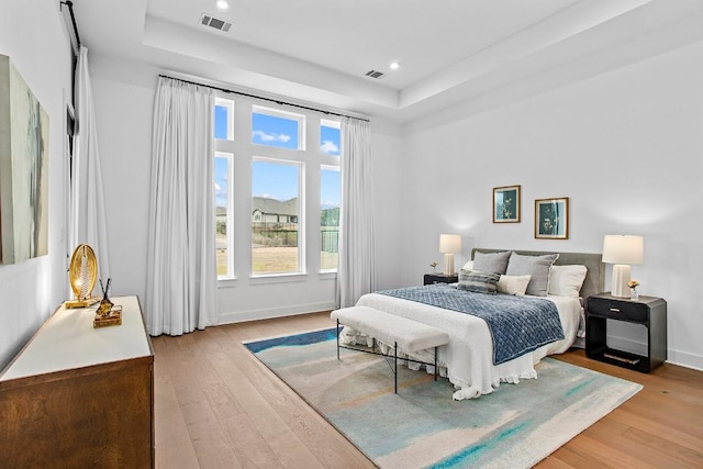 bedroom featuring light wood-style floors, a tray ceiling, and visible vents