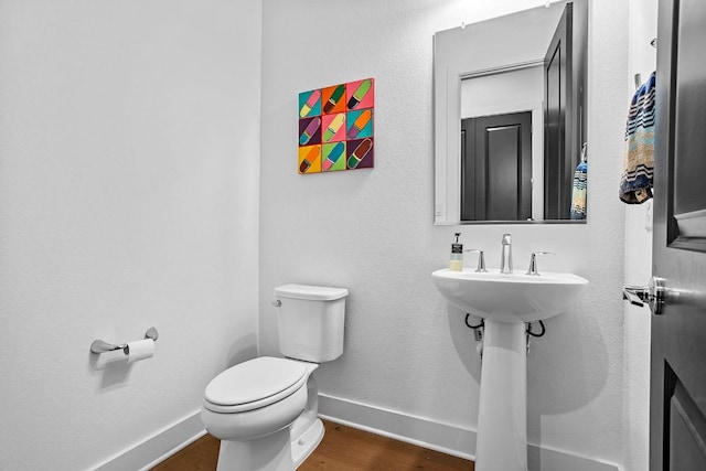 half bathroom with wood finished floors, toilet, and baseboards