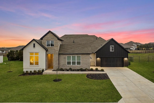 modern inspired farmhouse featuring stone siding, a yard, driveway, and fence