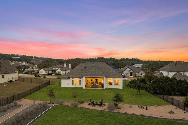 back of house at dusk featuring a yard, a fenced backyard, a residential view, and a patio