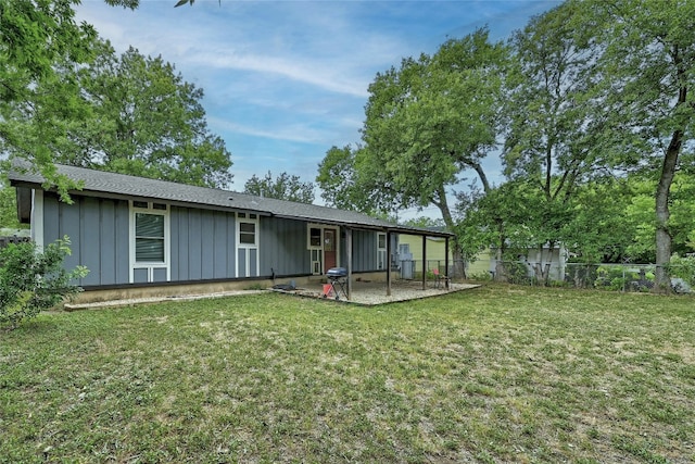 rear view of property featuring board and batten siding, a yard, a patio, and fence