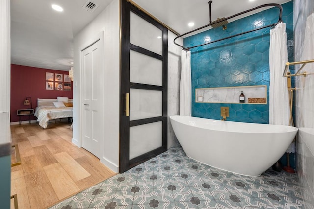 ensuite bathroom featuring visible vents, ensuite bath, wood finished floors, a freestanding bath, and tile walls