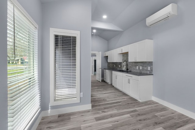 kitchen with dark countertops, backsplash, white cabinetry, a sink, and a wall mounted air conditioner