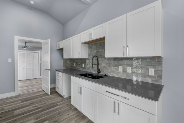 kitchen with dark countertops, vaulted ceiling, white cabinetry, and a sink