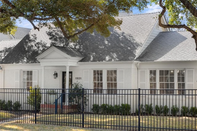 new england style home with covered porch, a shingled roof, and a fenced front yard