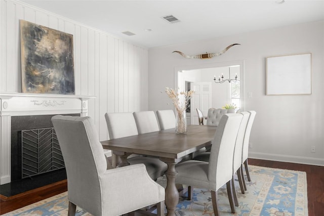 dining room featuring a fireplace, wood finished floors, visible vents, baseboards, and an inviting chandelier