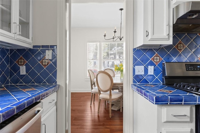 kitchen with tile countertops, appliances with stainless steel finishes, white cabinetry, wood finished floors, and wall chimney exhaust hood