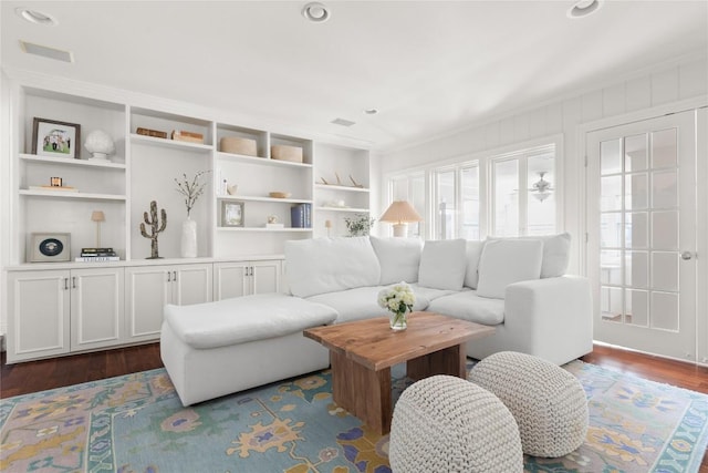 living area with dark wood-style floors, visible vents, and built in shelves