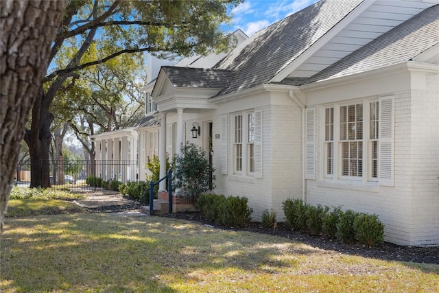 view of property exterior featuring a shingled roof, brick siding, a lawn, and fence