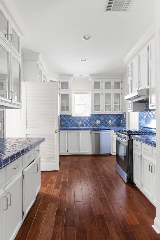 kitchen with stainless steel appliances, tile counters, visible vents, white cabinetry, and under cabinet range hood