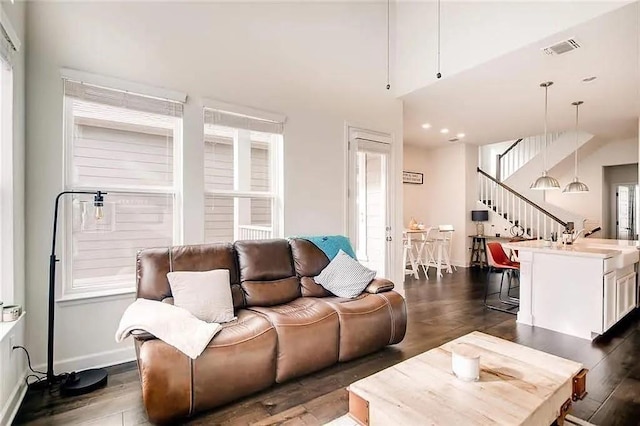 living room featuring dark wood-style floors, visible vents, stairway, and baseboards