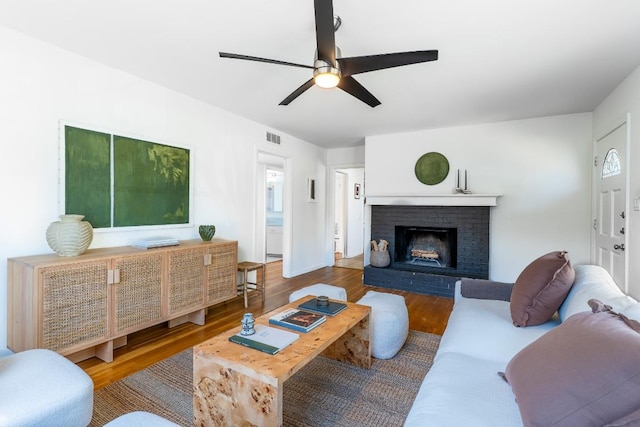 living room with ceiling fan, a brick fireplace, wood finished floors, and visible vents