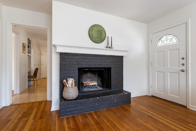 foyer featuring a brick fireplace, wood finished floors, and baseboards