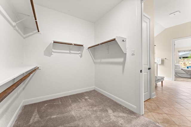 spacious closet featuring vaulted ceiling, light tile patterned floors, visible vents, and light colored carpet