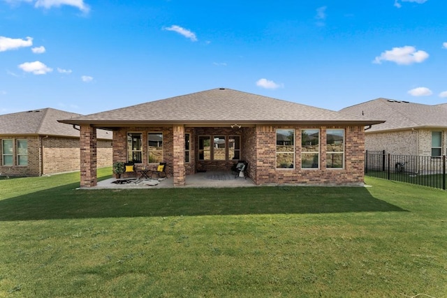 back of property featuring a yard, brick siding, roof with shingles, and fence