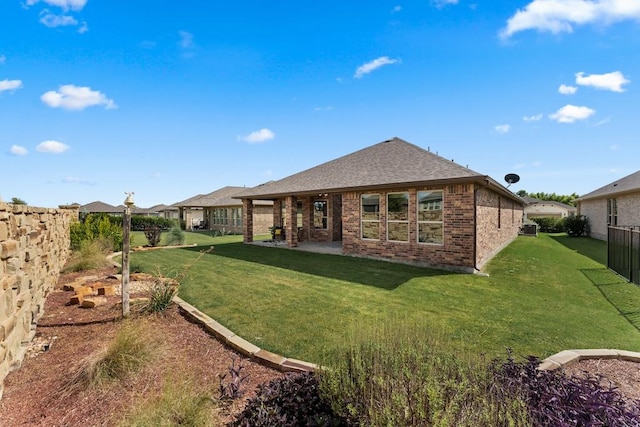 back of property featuring a shingled roof, brick siding, a lawn, and a patio